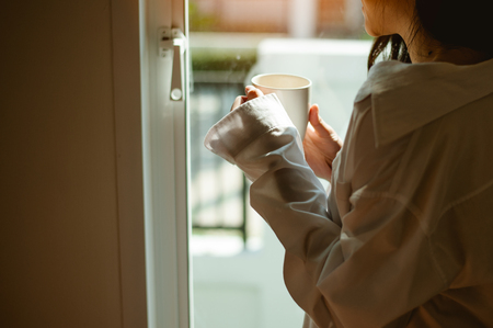 Woman holding a glass of coffee in the window in the morning.の写真素材