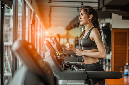 Portrait of Fitness woman running on treadmill in gym listening to music.exercising concept.fitness...