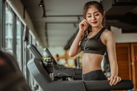 Portrait of Fitness woman running on treadmill in gym listening to music.exercising concept.fitness and healthy lifestyle.の写真素材