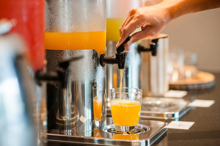close up hand pulling down the lever of juice dispenser for fresh orange juice.の写真素材