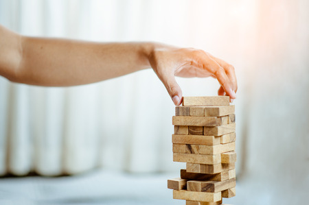 hand  pulling out or placing wood block on the tower in modern office. plan and strategy in business. blur for background.の写真素材