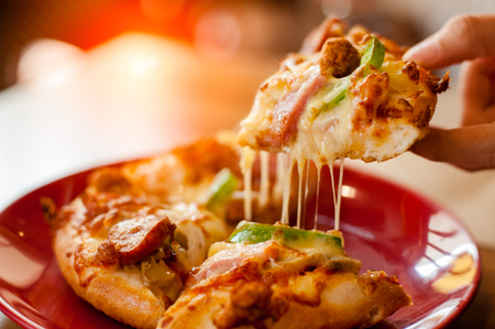A slice of pizza in hand.Hot pizza slice with melting cheese.の写真素材
