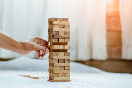 hand  pulling out or placing wood block on the tower in modern office. plan and strategy in business. blur for background.の写真素材