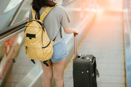 Young woman pulling and use smartphone suitcase in modern airport terminal. Travelling guy with his luggage while waiting for transport. Rear view. Copy spaceの写真素材