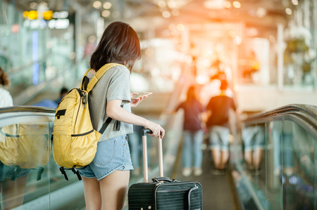 Young woman pulling suitcase in modern airport terminal. Travelling guy with his luggage while waiting for transport. Rear view. Copy spaceの写真素材