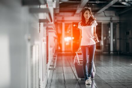 Young woman pulling suitcase in modern airport terminal. Travelling with her luggage while waiting for transport. Rear view.の写真素材