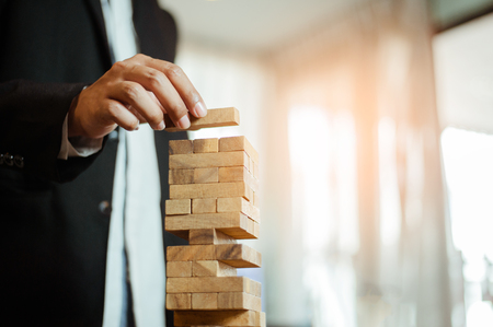 business man hand  pulling out or placing wood block on the tower in modern office. plan and strategy in business. blur for background.の写真素材