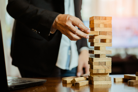 business man hand  pulling out or placing wood block on the tower in modern office. plan and strategy in business. blur for background.の写真素材