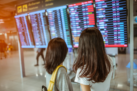 Two women in international airport terminal, looking at information board, checking her flight.の写真素材