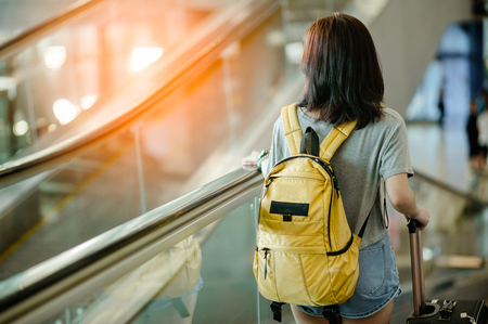 Young woman pulling suitcase in modern airport terminal. Travelling guy with his luggage while waiting for transport. Rear view. Copy spaceの写真素材