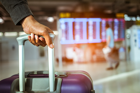 close up man hand touching baggage for check in at flight timetable in international airport.の写真素材