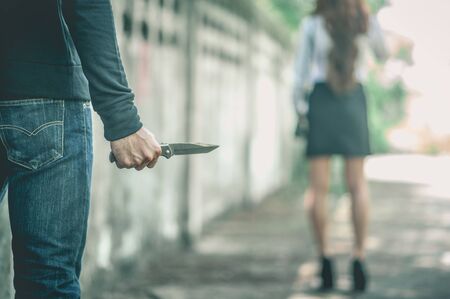 A bandit holds a knife. In order to attack and steal a woman's belongings from the back.の写真素材