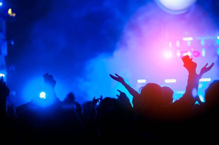 silhouettes of hand in concert.Light from the stage.confetti.the crowd of people silhouettes with their hands up.ribbonの写真素材