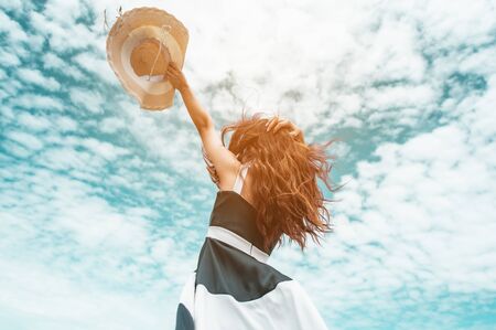 Happy asian women with holding hat stand to receive the wind and enjoy life on the beach vacation. beach, summer, liftstyle, positive mood, travel, relax concept.の写真素材