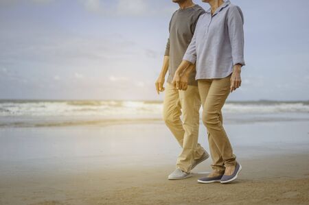 Senior lovers walk hand in hand at the beach at sunrise, plan life insurance at retirement concept.の写真素材