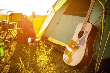 The guitar focus is on the side of the tent of the group of friends who enjoy hiking in the forest are looking for a tent to relax. Hiking, hiker, asian, forest, camping, activity concept.の写真素材