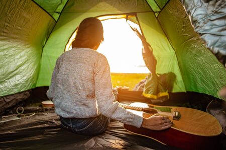 The woman asian who just woke up inside the tent was watching the sunrise in the morning as a holiday activity in the forest path autumn season. Hiking, hiker, alone, forest, camping, activity concept.の写真素材