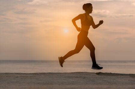 silhouette of  runner woman in running workout training at sunset beach.Silhouette of an athletic woman running on the beach during sunset time.の写真素材