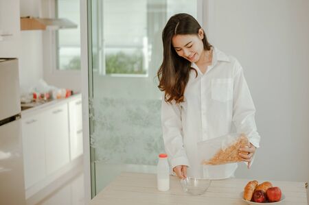 Young woman asia wake up refreshed in the morning and relaxing eat coffee, cornflakes, bread and apple for breakfast at house on holiday. Asian, asia, relax, breakfast, refresh, lifestyle concept.の写真素材