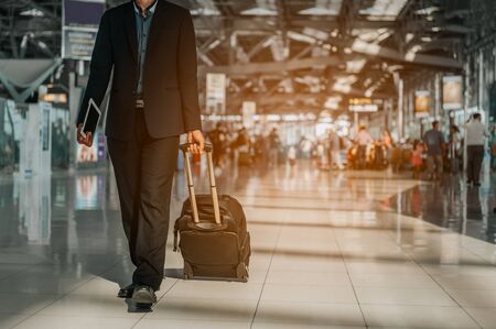 Businessman with hand luggage walking in airport terminal.Businessman carrying suitcase while walking through a passenger departure terminal in airport. Businessman traveler journey business travel.の写真素材