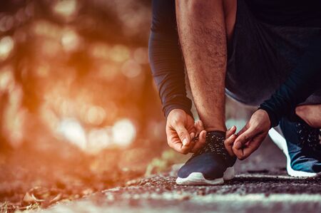 Fitnessman tying shoe laces. Closeup of man sport fitness runner getting ready for jogging.Man jogging in the morning.の写真素材