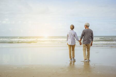 Senior couple standing on the beach holding hands at sunrise, plan life insurance at retirement concept.の写真素材