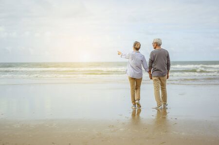 Senior couple standing on the beach holding hands at sunrise, plan life insurance at retirement concept.の写真素材