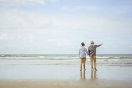 Senior couple standing on the beach holding hands at sunrise, plan life insurance at retirement concept.の写真素材