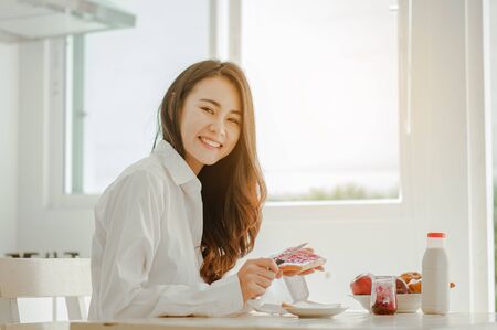 Young woman asia wake up refreshed in the morning and relaxing eat coffee, cornflakes, bread and apple for breakfast at house on holiday. Asian, asia, relax, breakfast, refresh, lifestyle concept.の写真素材