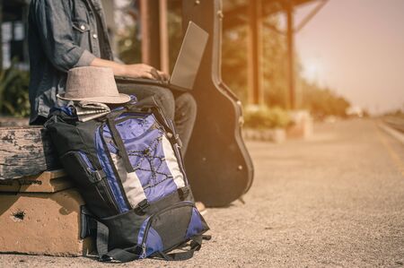 A young male traveler traveling alone sitting on a laptop while waiting for the train There is a backpack and a hat at the train station on summer holidays and the travel and tourism conceptの写真素材