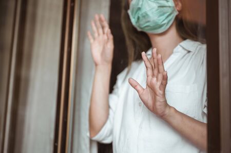 Woman wearing mask protection at the window wait for epidemic situation to improve soon at home. Coronavirus, covid-19, Work from home (WFH), Social distancing, Quarantine, Prevent infection concept.の写真素材