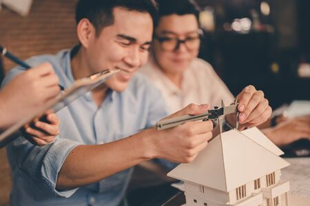 Male architect hands measuring and making model house with them team on the desk at sunset. Engineer, Engineering, Architecture, Design, Planning, Occupation concept.の写真素材