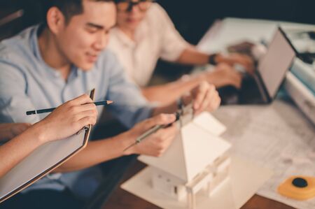 Male architect hands measuring and making model house with them team on the desk at sunset. Engineer, Engineering, Architecture, Design, Planning, Occupation concept.の写真素材
