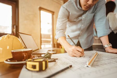 Close up of male architect hands writing model on the desk. Blurred behind team of engineer discussing of construction plan. Engineer, Engineering, Architecture, Design, Planning, Occupation concept.の写真素材