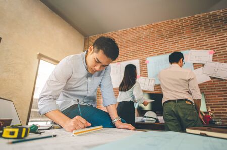 Close up of male architect hands writing model on the desk. Blurred behind team of engineer discussing of construction plan. Engineer, Engineering, Architecture, Design, Planning, Occupation concept.の写真素材