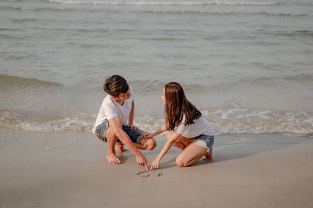 Romantic couple sitting and writing on the sand at the beach in sunset. plan life insurance at future concept. couple, love, beach, romantic, summer, lifestyle concept.の写真素材