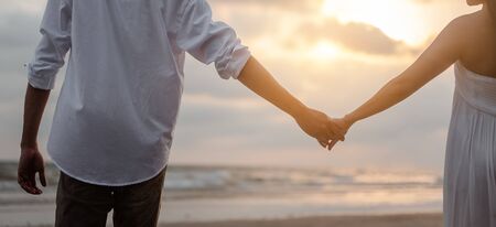 Rear view of couple standing holding hands each other while at beach at sunrise, plan life at future concept. couple, lover, beach, romantic, summer, lifestyle concept.の写真素材