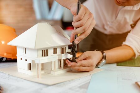 Close up of male architect hands measuring and making model house on the desk at sunset. Engineer, Engineering, Architecture, Design, Planning, Occupation concept.の写真素材