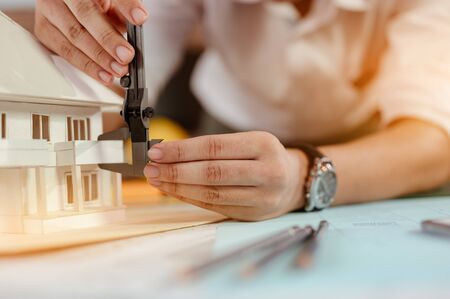 Close up of male architect hands measuring and making model house on the desk at sunset. Engineer, Engineering, Architecture, Design, Planning, Occupation concept.の写真素材
