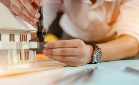 Close up of male architect hands measuring and making model house on the desk at sunset. Engineer, Engineering, Architecture, Design, Planning, Occupation concept.の写真素材