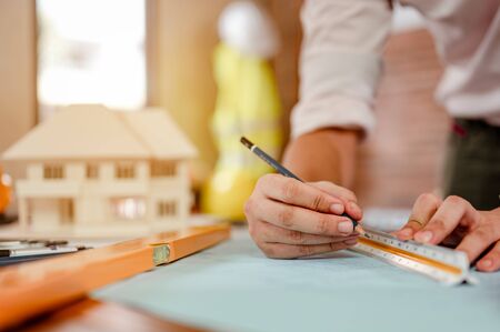 Close up of male architect hands measuring and making model house on the desk at sunset. Engineer, Engineering, Architecture, Design, Planning, Occupation concept.の写真素材
