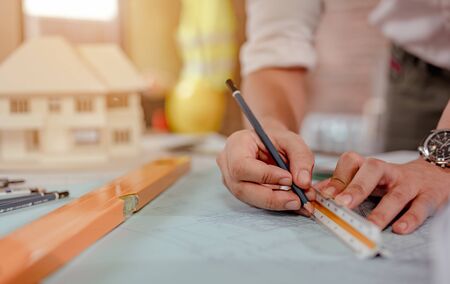 Close up of male architect hands measuring and making model house on the desk at sunset. Engineer, Engineering, Architecture, Design, Planning, Occupation concept.の写真素材