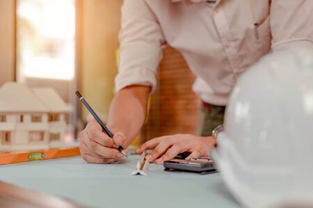 Close up of male architect hands measuring and making model house on the desk at sunset. Engineer, Engineering, Architecture, Design, Planning, Occupation concept.の写真素材