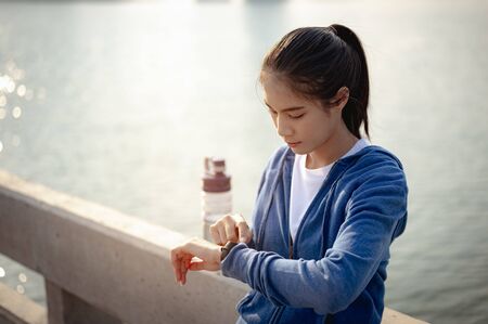 Young woman check the pulse via a smartwatch after jogging a morning workout in the city. A city...