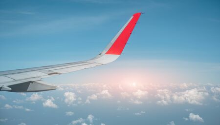 The wings of the plane are flying in the turquoise sky and the orange light sun. Airplane, Travel, Wing, Airport, Sky, technology concept.の写真素材