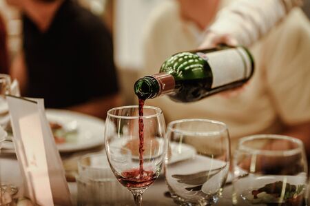 Waitress is pouring red wine in glasses for wine tasting event on the table in restaurant . Blurred background. wine, tasting, pour, bartender, beverage, dinner concept.の写真素材
