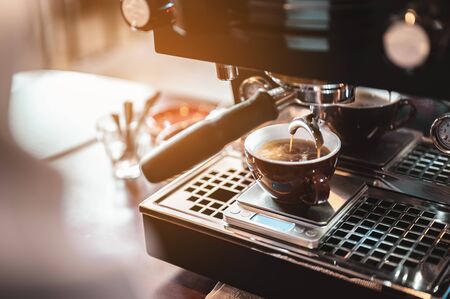 Close-up coffee maker that is professionally extracting coffee by barista with a deep white glass in the evening sun light. coffee, extraction, deep, machine, make, barista concept.の写真素材