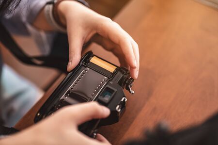 Close-up hands of woman putting a roll of film into a retro camera on brown wooden table in the morning. Film, camera, classic, put, Vintage, lifestyle concept.の写真素材