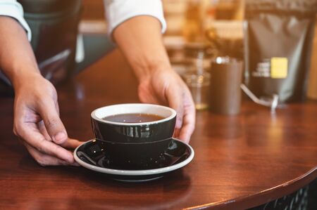 Close up of hands barista man serving coffee in coffee shop. male hands placing a cup of coffee on table. Coffee, Barista, extraction, serve, cafe, lifestyle concept.の写真素材