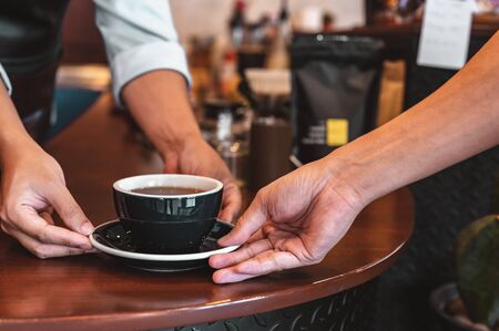 Close up of hands barista man serving coffee in coffee shop. male hands placing a cup of coffee on table. Coffee, Barista, extraction, serve, cafe, lifestyle concept.の写真素材